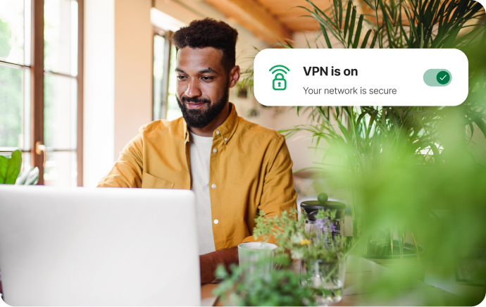 Kasvien ympäröimä mies katsoo hymyillen kannettavaa tietokonetta